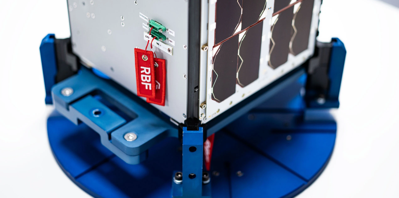 Close-up of a 16 cubesat mounted on a test fixture with remove-before-flight safety tag attached